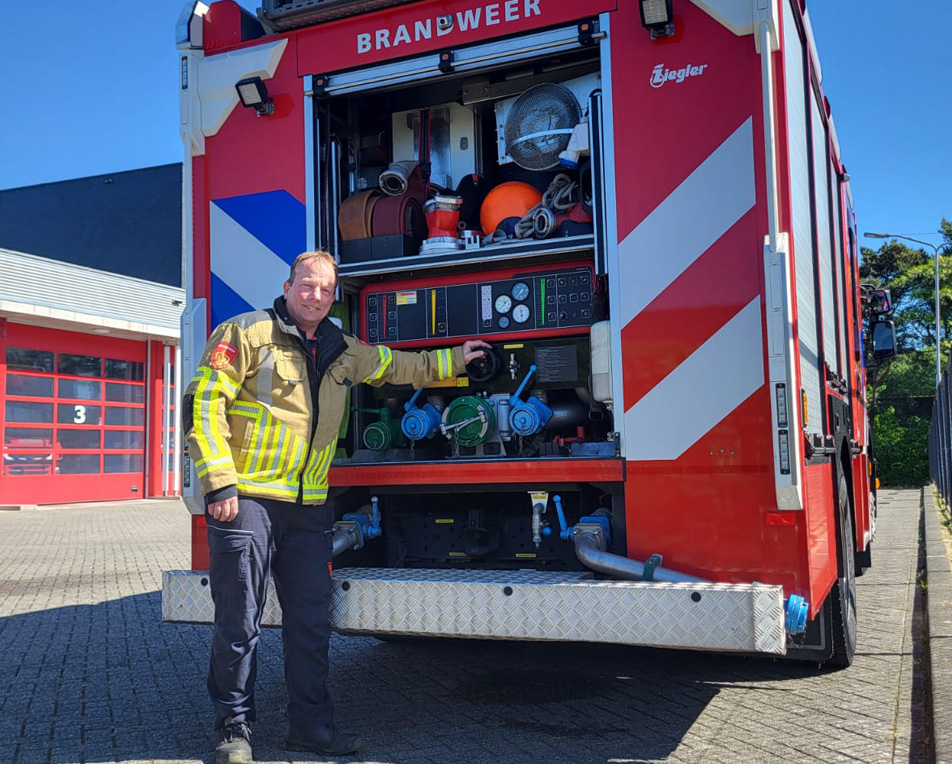 Brandweerman en Yonder cursist Mario bij brandweerwagen met geopende uitrustingskast bij kazerne