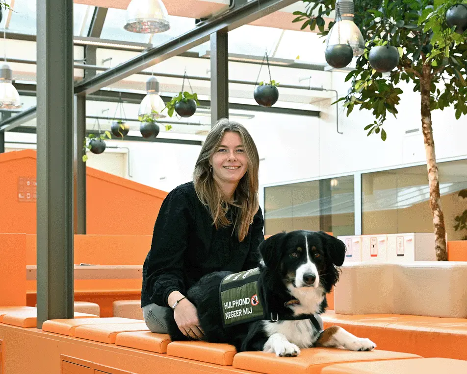 Vrouw zit op oranje banken, in een lichte ruimte met veel oranje, samen met hond.