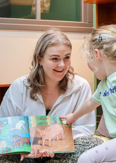 Vrouw in witte trui leest een kinderboek voor aan een klein kind.