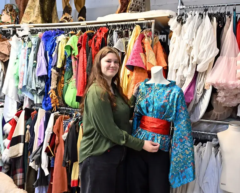 Vrouw met groen T-shirt staat bij een paspop voor een groot kledingrek.