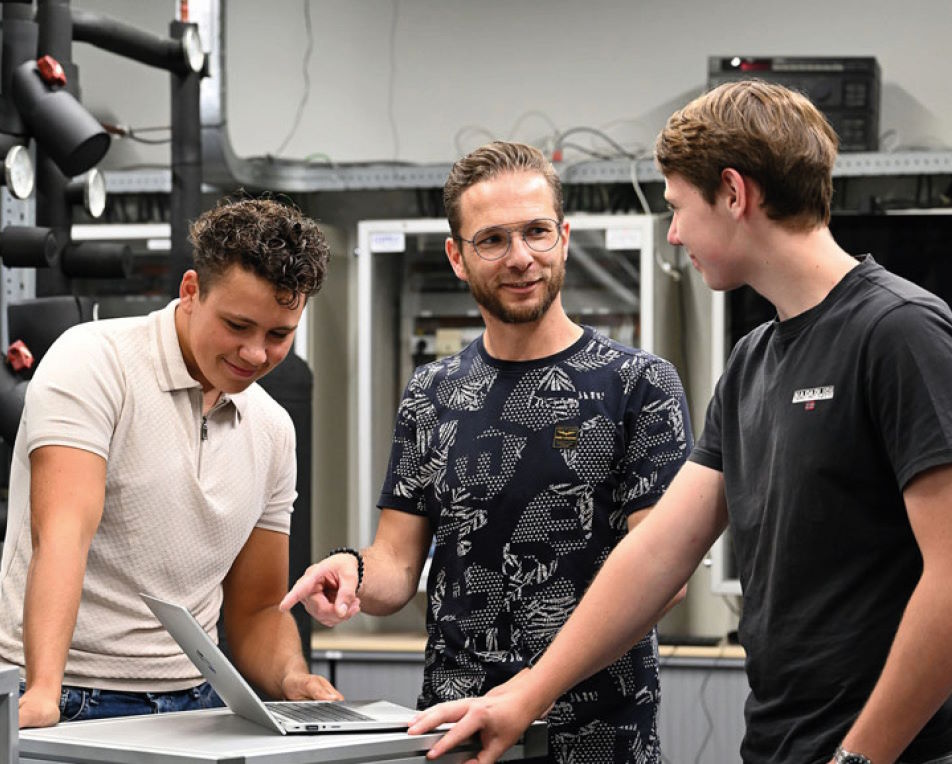 Drie jongens kijkend naar een laptop in een werkruimte.