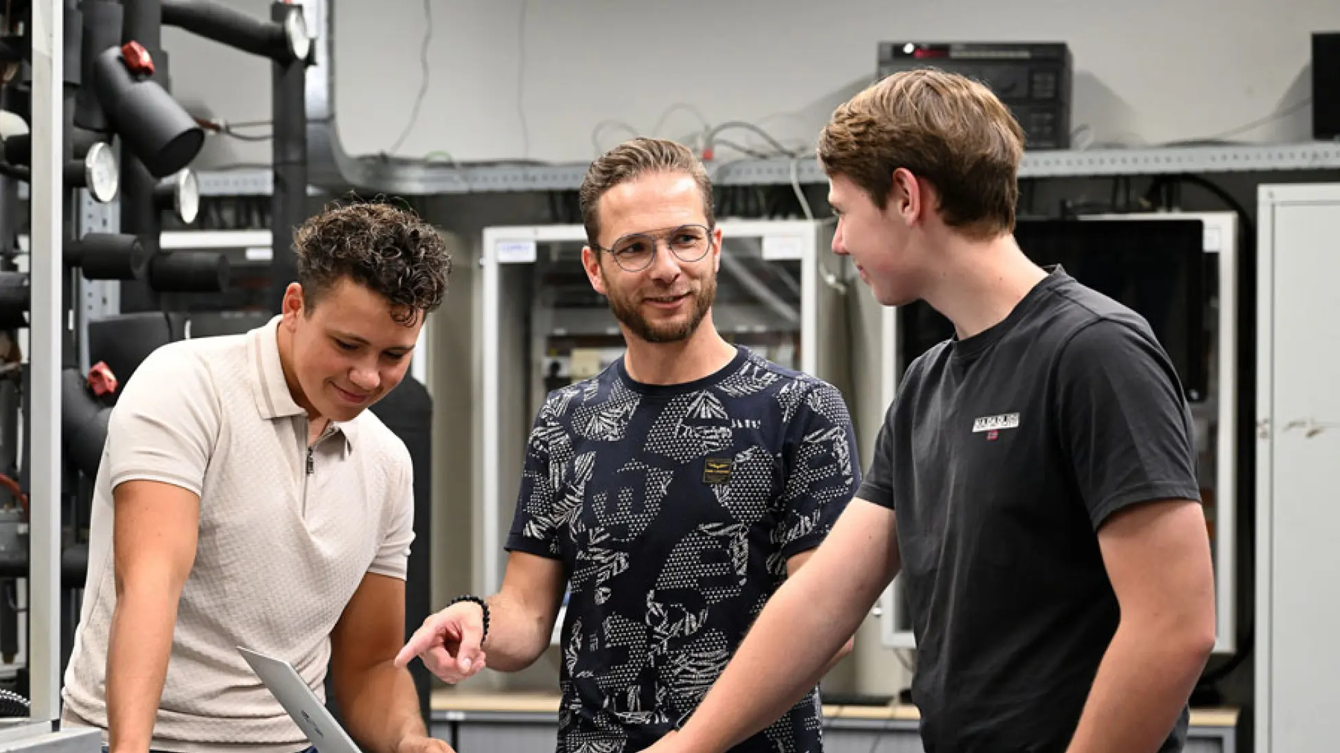 Drie jongens kijkend naar een laptop in een werkruimte.