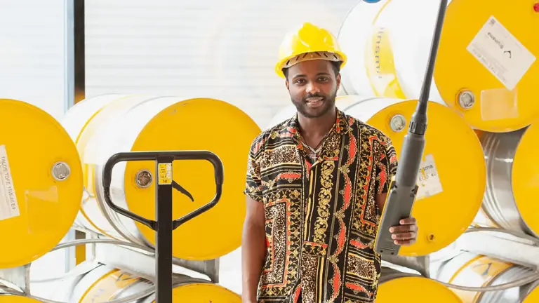 Man met gele veiligheidshelm staat voor grote gele tonnen.